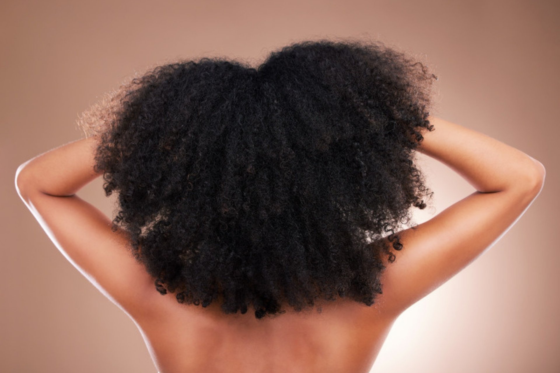 Woman with a natural afro seen from behind with her arms raised, showing smooth skin on her back